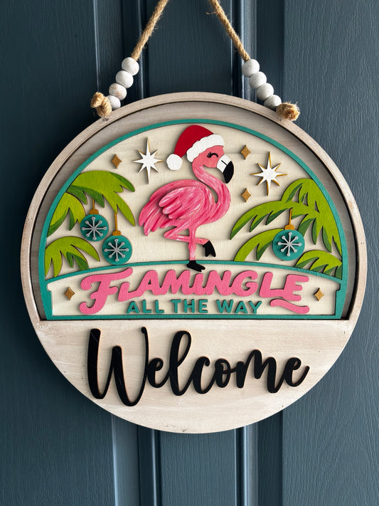 Pink flamingo in a Santa hat between palm trees with ornaments and Flamingle All the Way lettering, displayed in welcome sign base